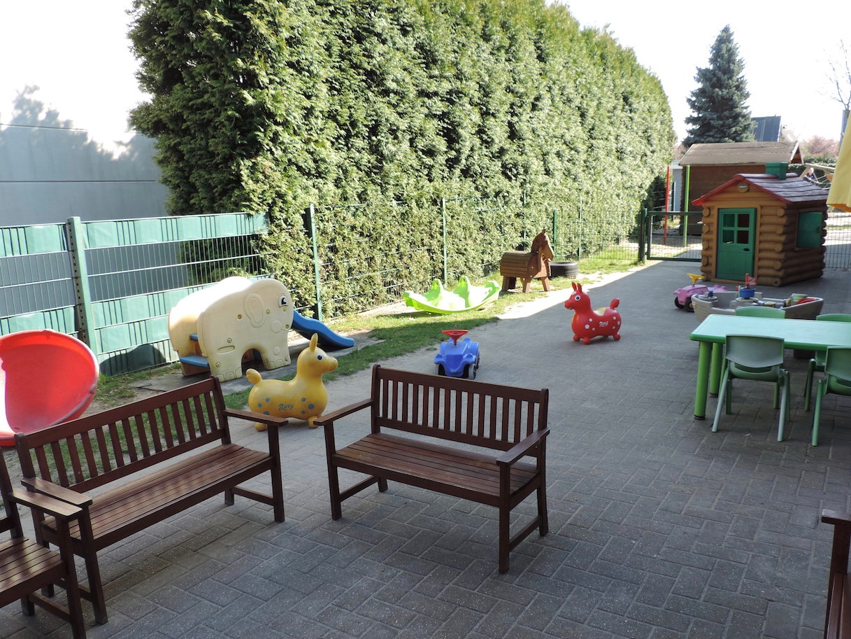 Terrasse der grünen Gruppe mit Sandkasten, einer Hütte und diversen Spielzeug 
